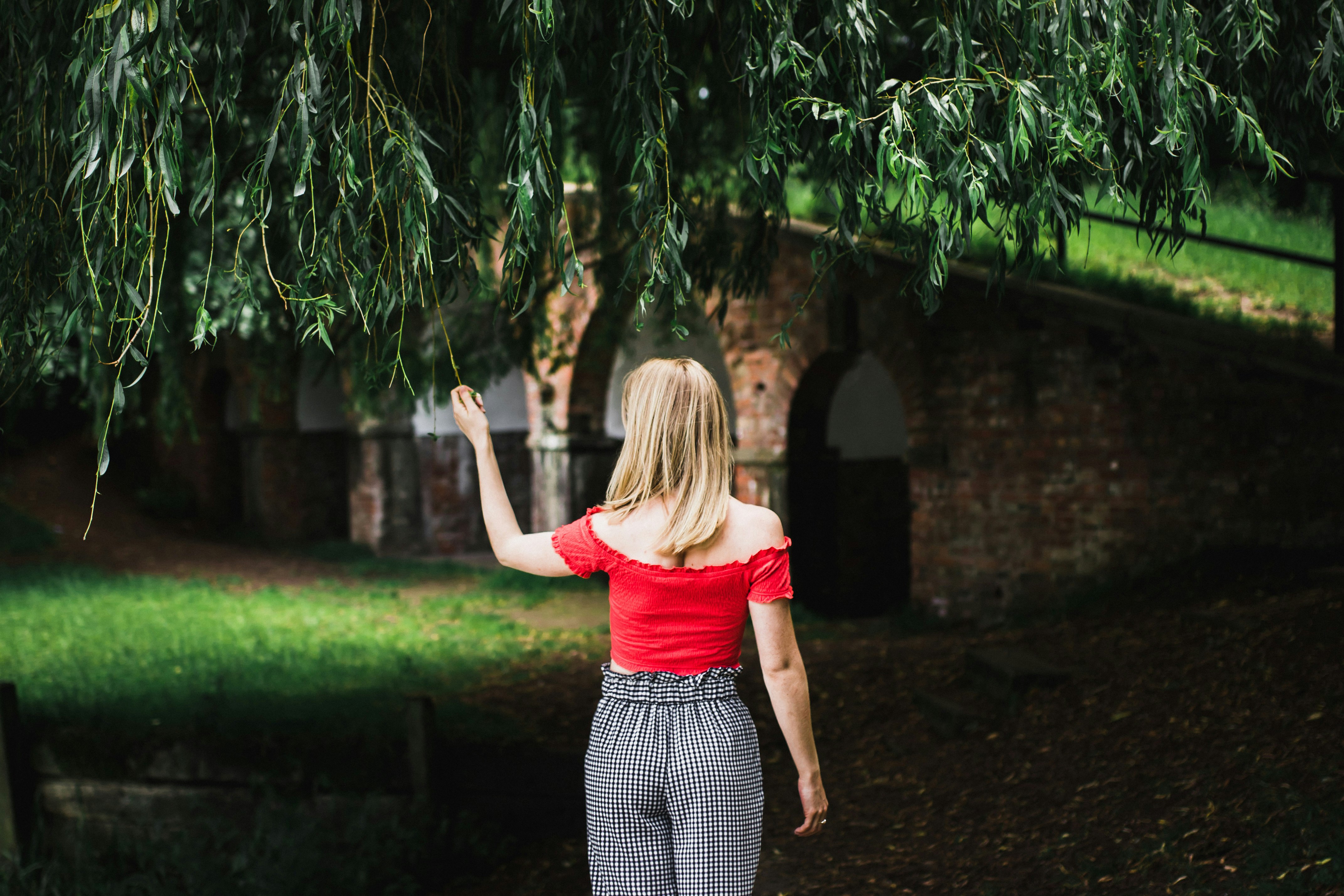 woman standing grabbing green tree leaf wearing red t-shirt